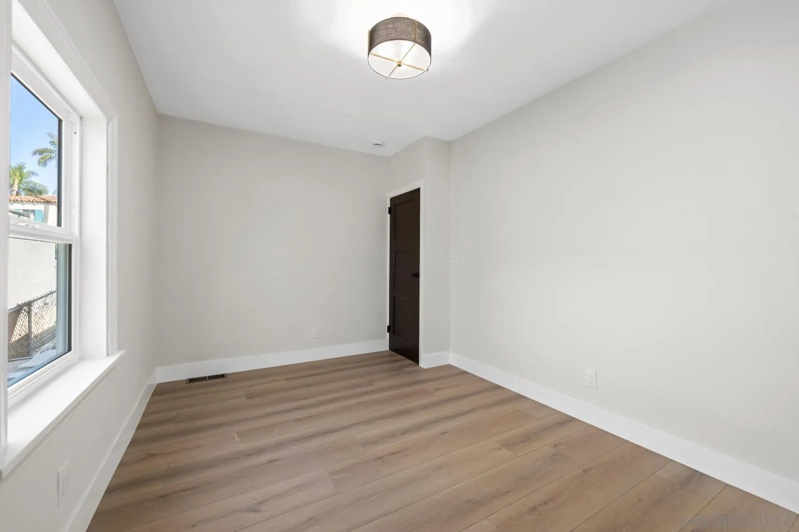 Empty room with light wood-look flooring, a large window, and a dark brown door.