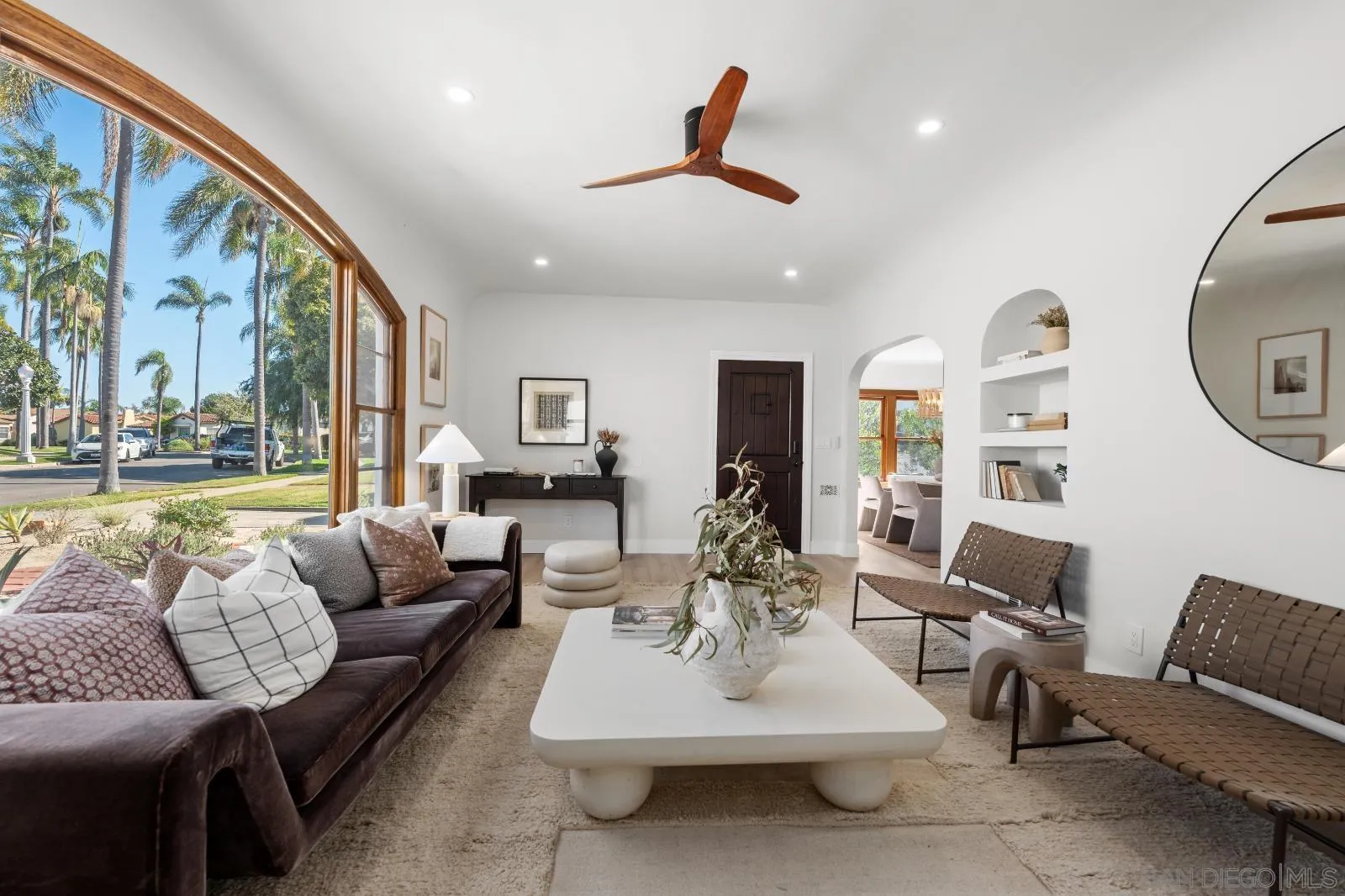 Living room with a sweeping arched window, palm-lined street view, and contemporary furnishings.