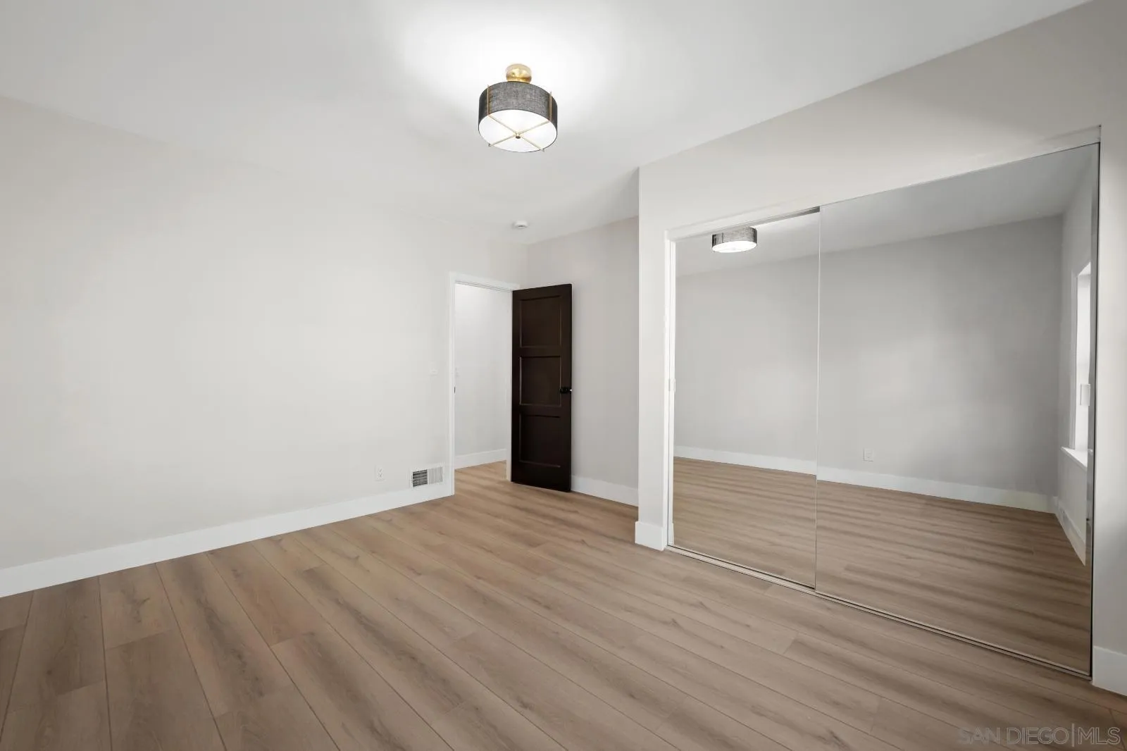 Empty bedroom with light wood floors and mirrored sliding closet doors.