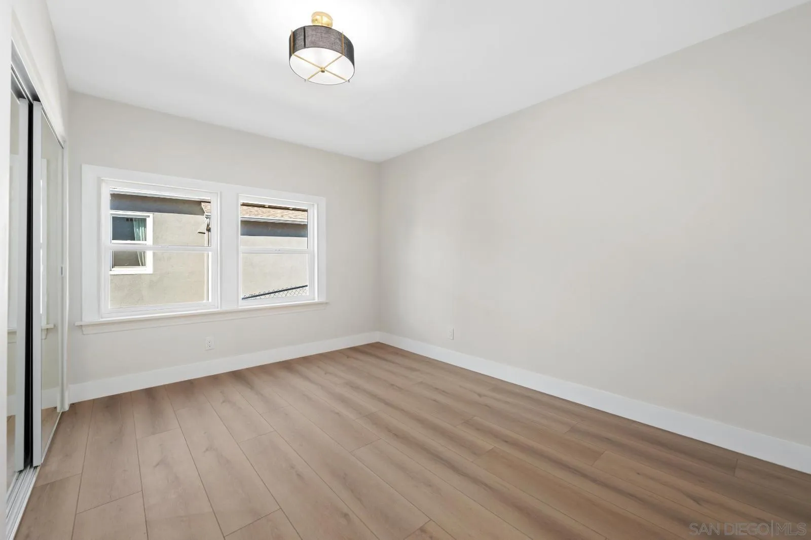 Empty room with light plank flooring, two windows, and a modern ceiling light.