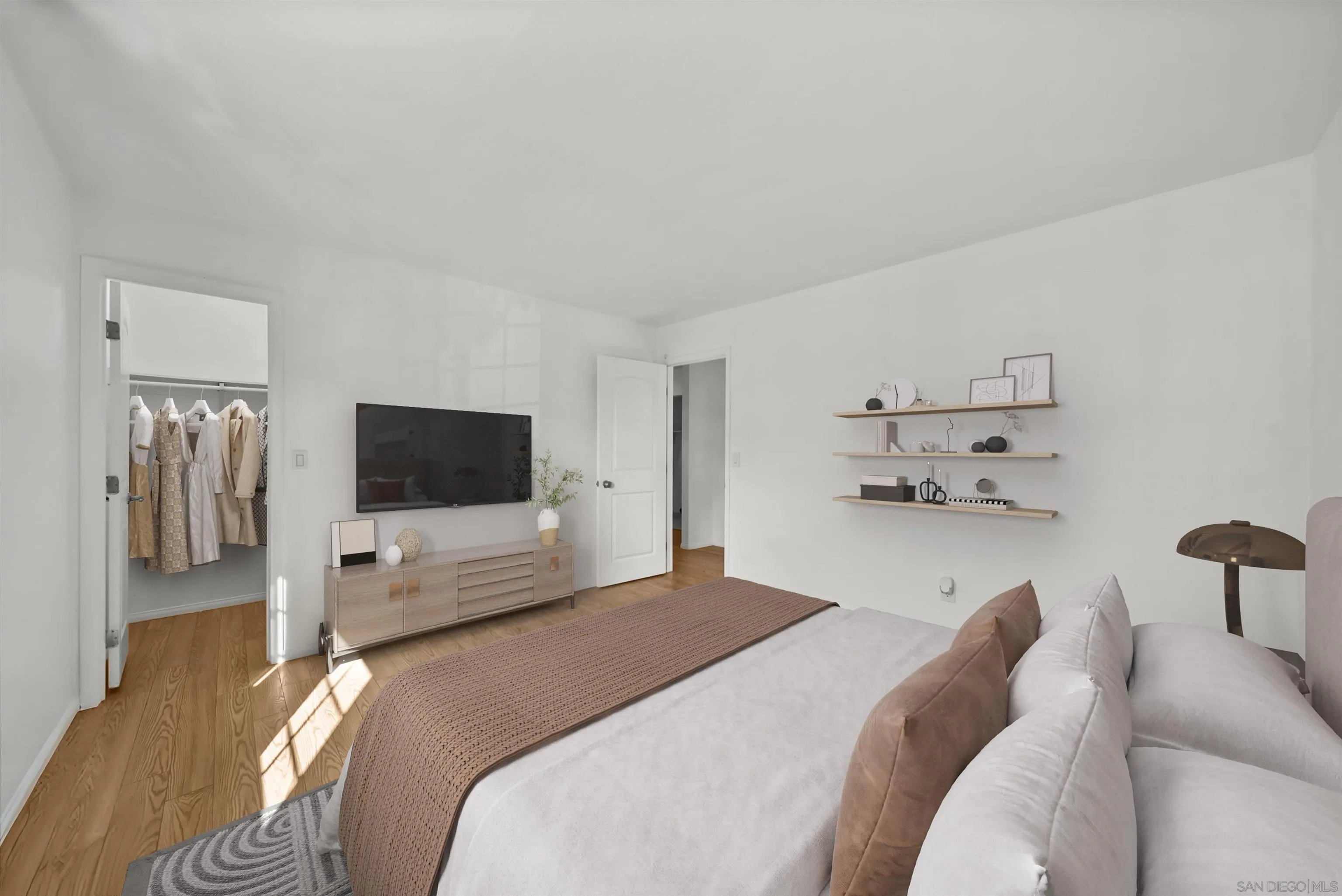 Staged bedroom with a large bed, warm wood floors, wall-mounted TV, and open closet.
