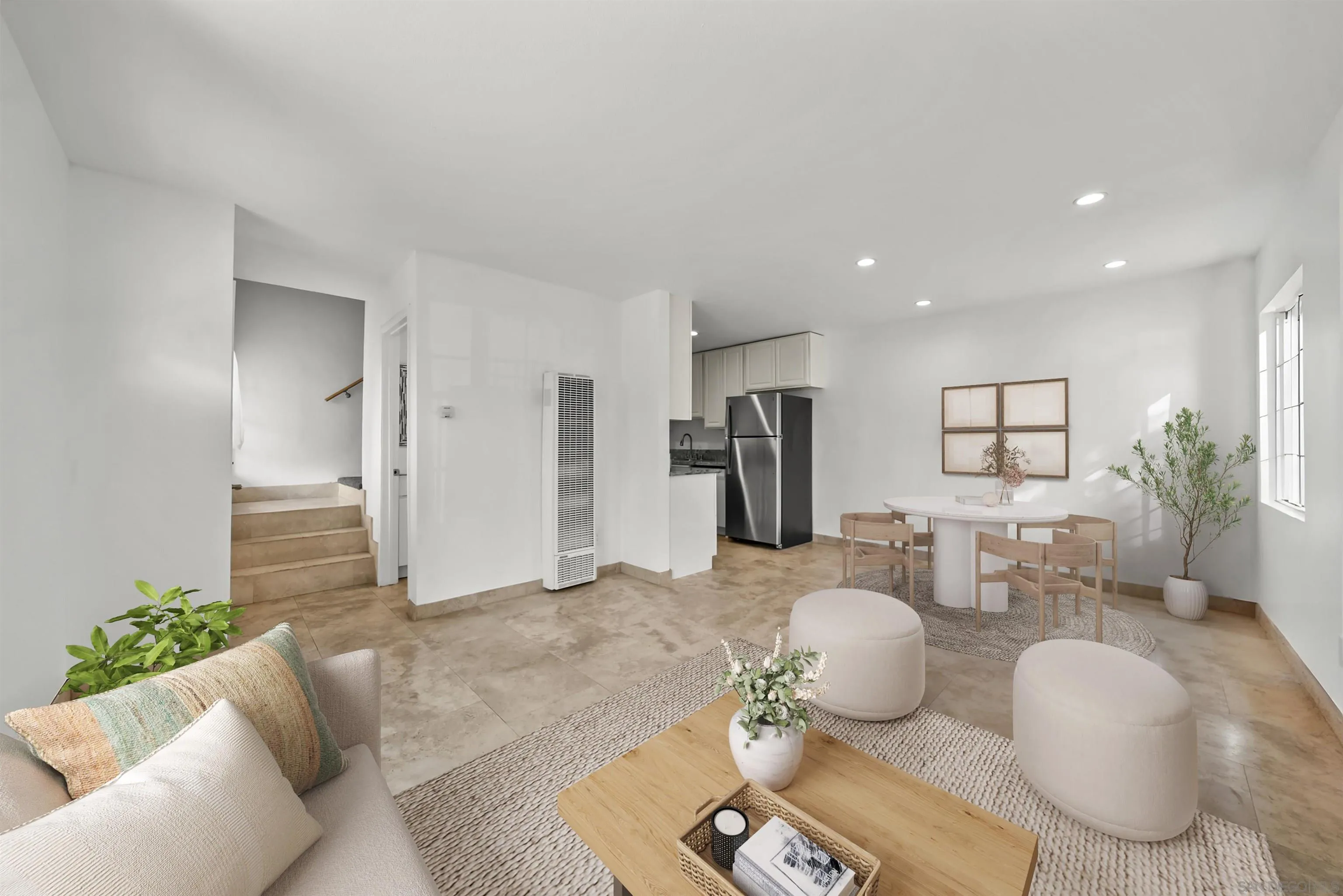 Staged open-plan living and dining area with a compact kitchen, stainless steel refrigerator, and large windows.