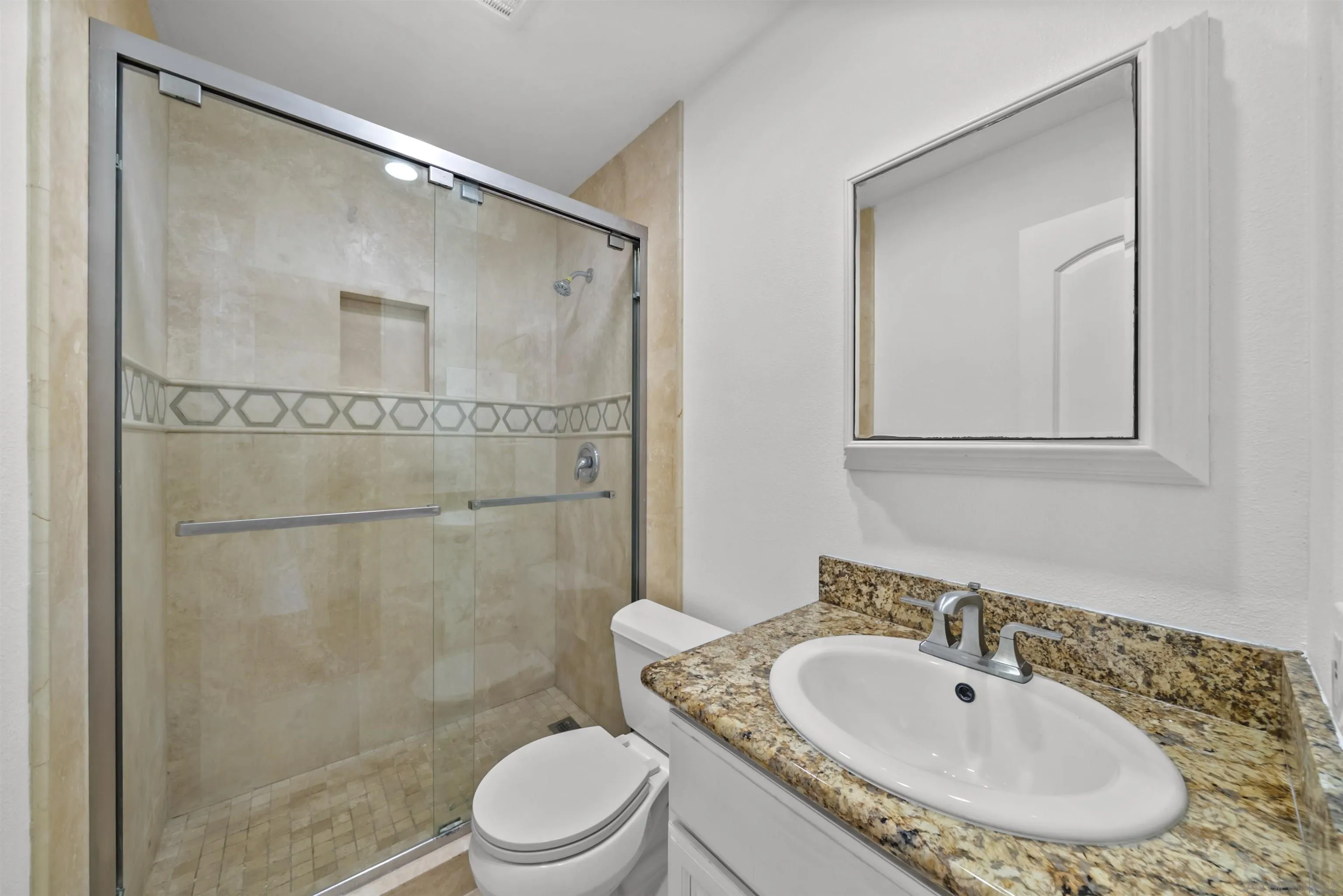 Bathroom with a glass-enclosed tiled shower, geometric accent band, and granite vanity.