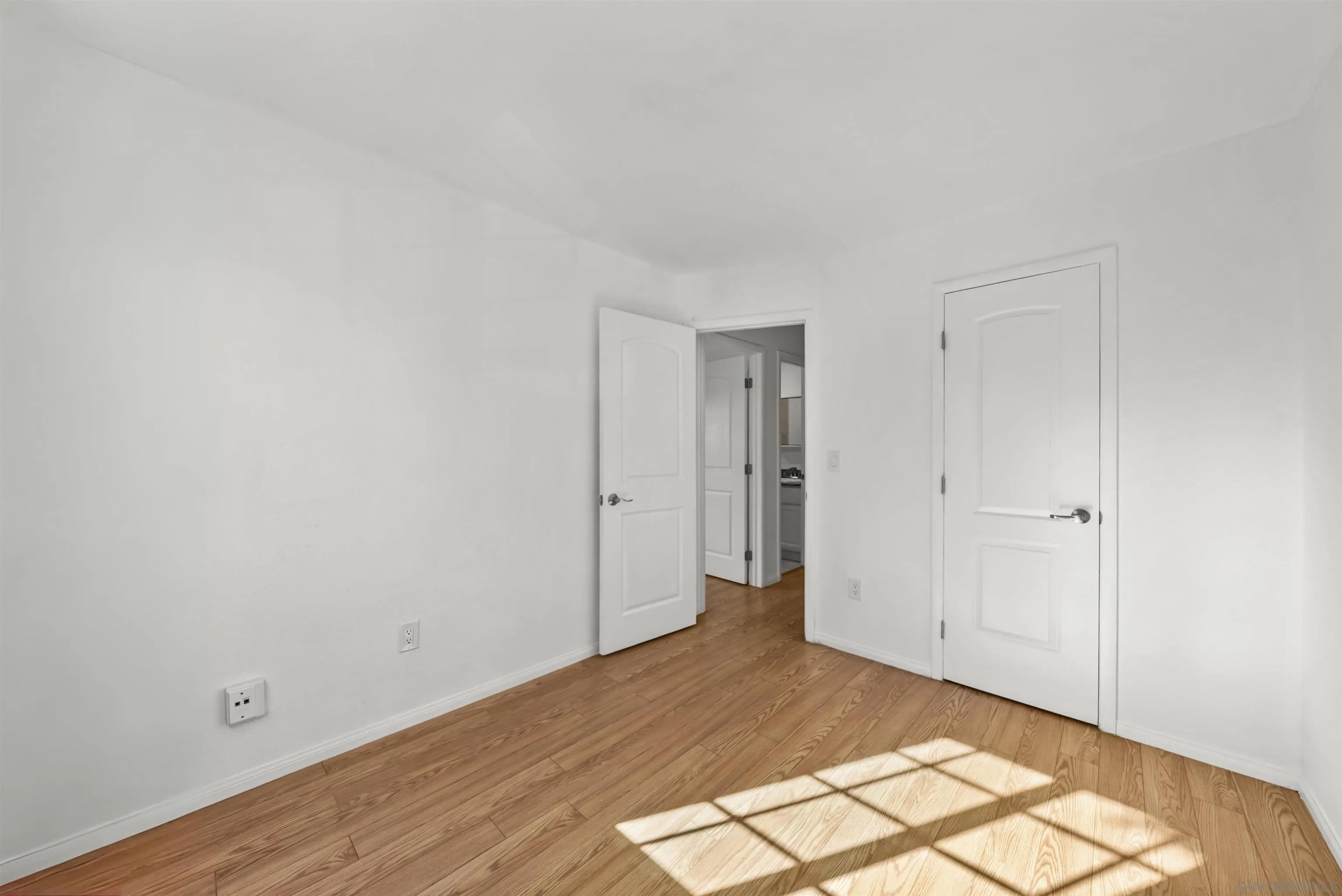 Empty room with hardwood floors, white walls, and sunlight casting a grid-shaped shadow.