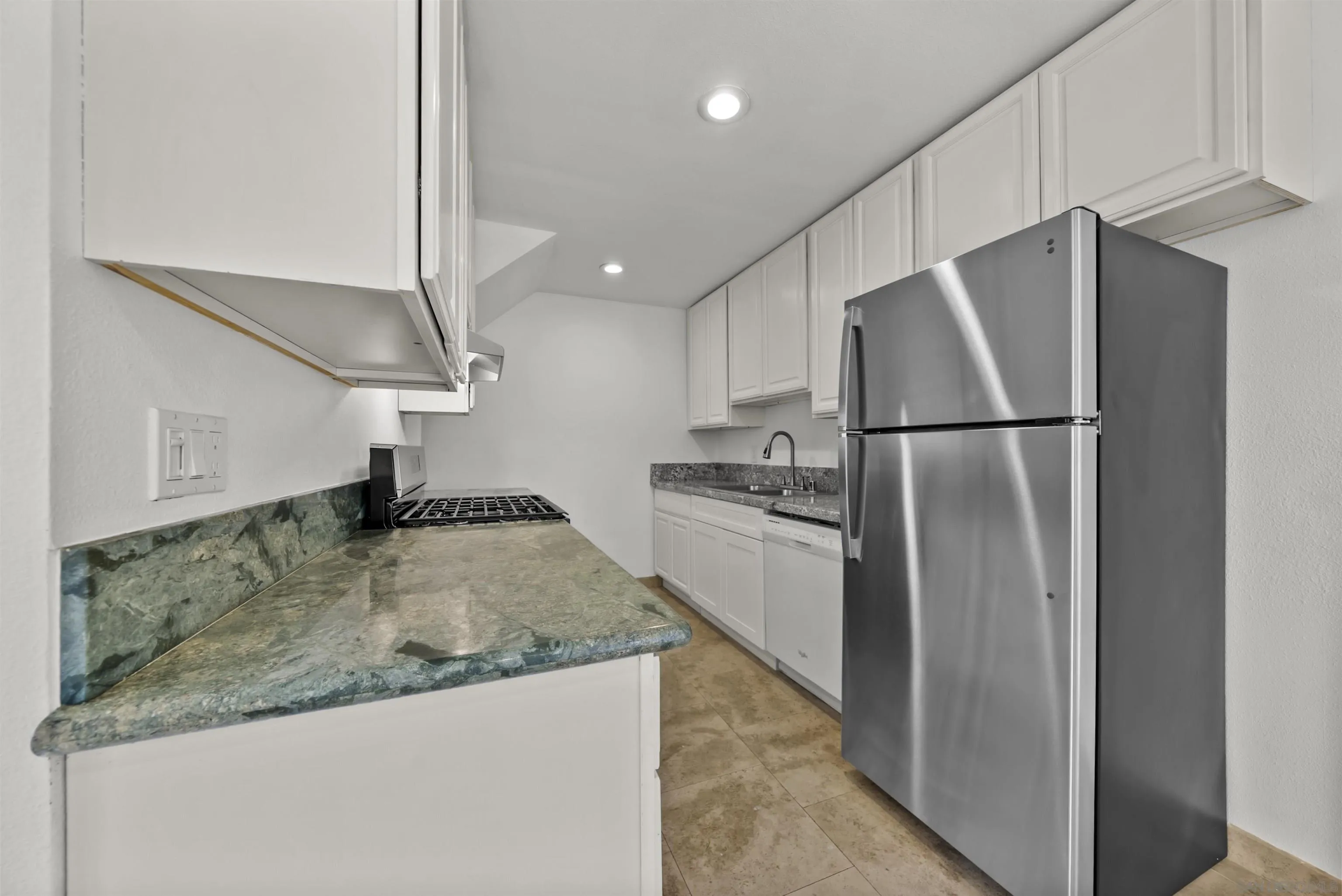 Kitchen with white cabinets, stone counters, a gas range, and a stainless steel refrigerator.