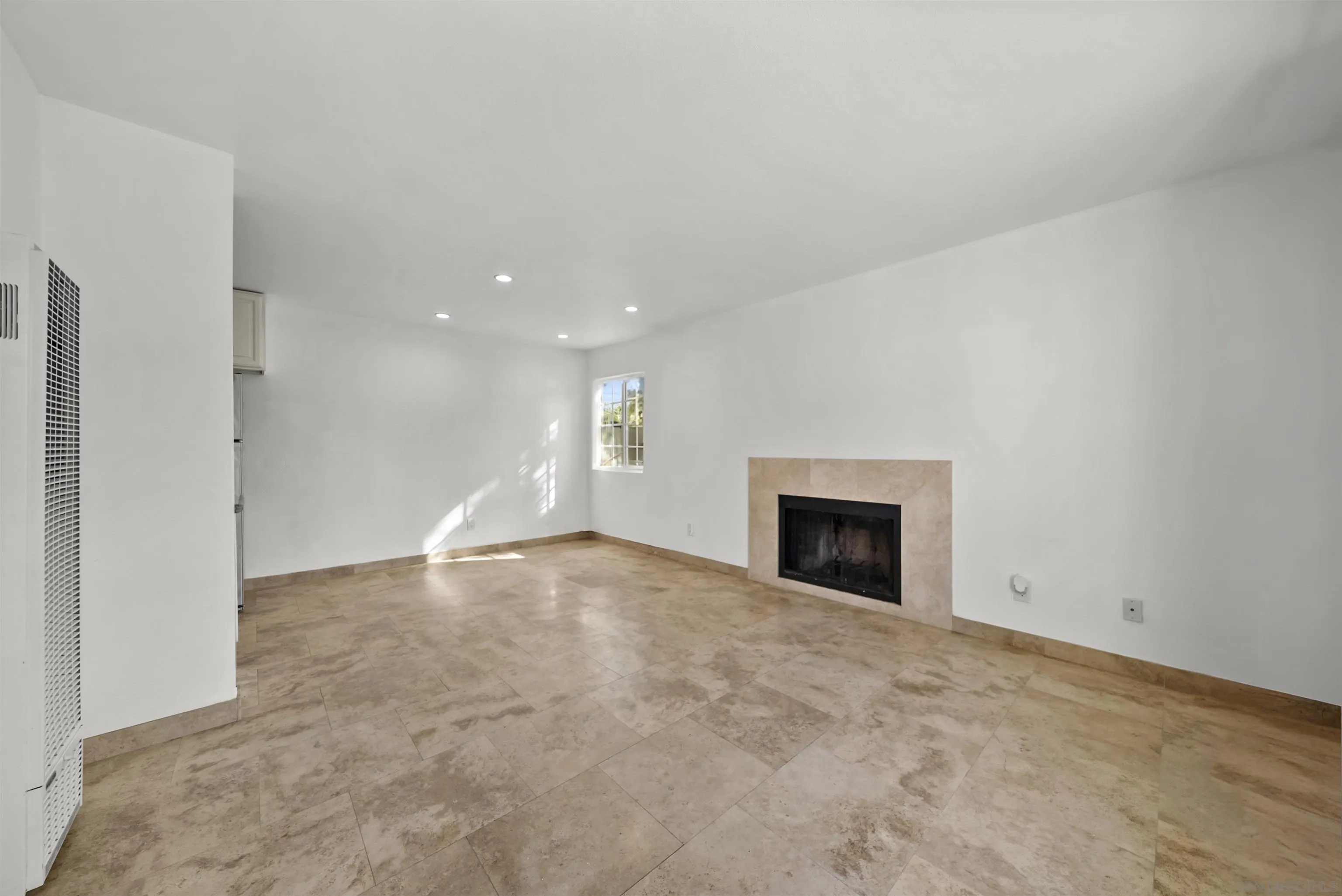 Empty living room with beige tile floors and a stone-surround fireplace.