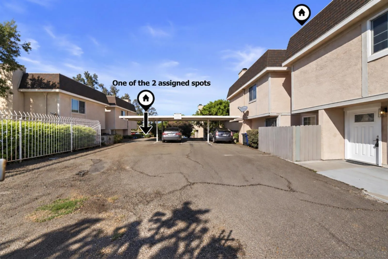Assigned parking spot marked by an arrow in the paved lot between beige stucco residences.