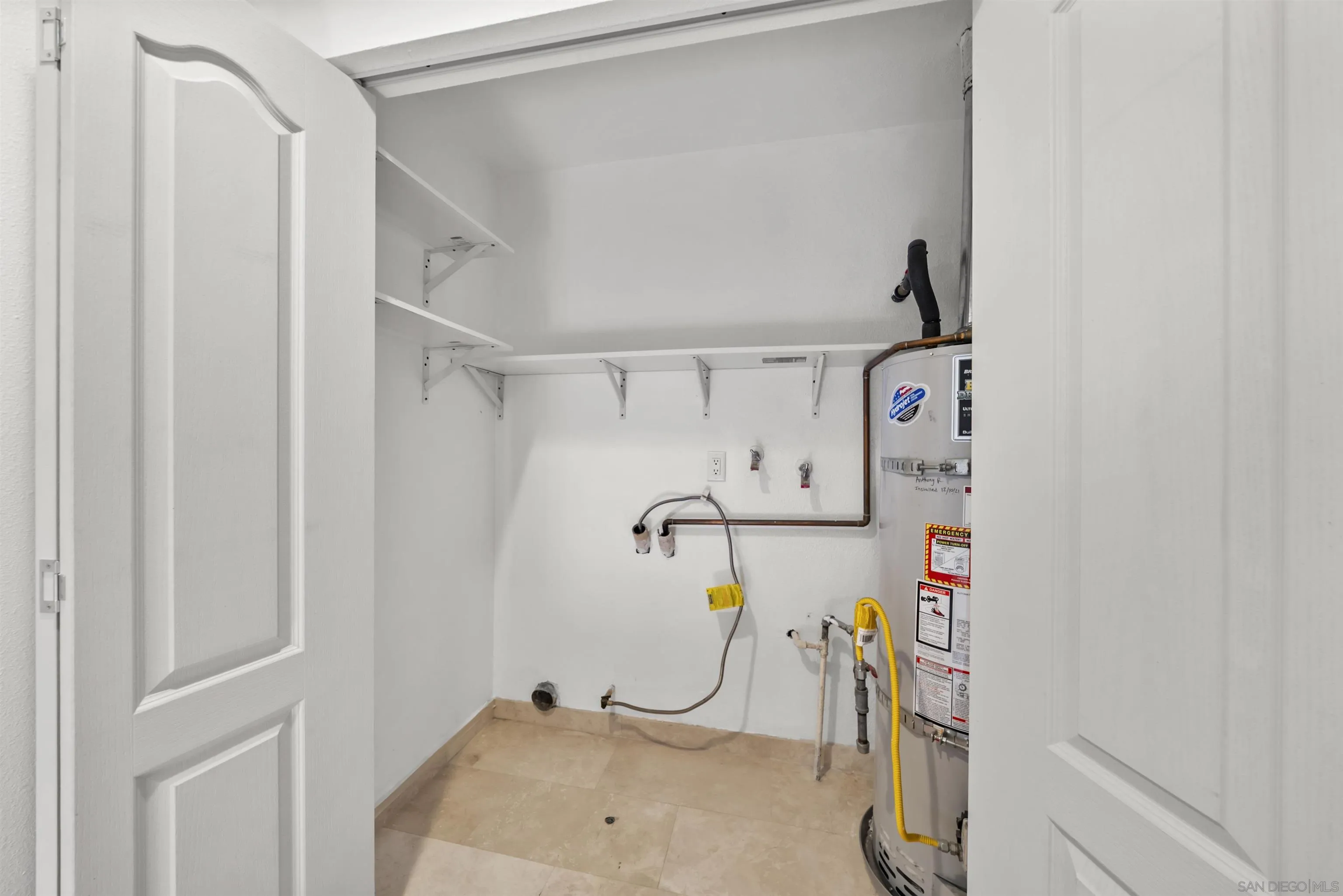 Utility closet with a tank water heater, laundry hookups, exposed plumbing, and wall shelves.