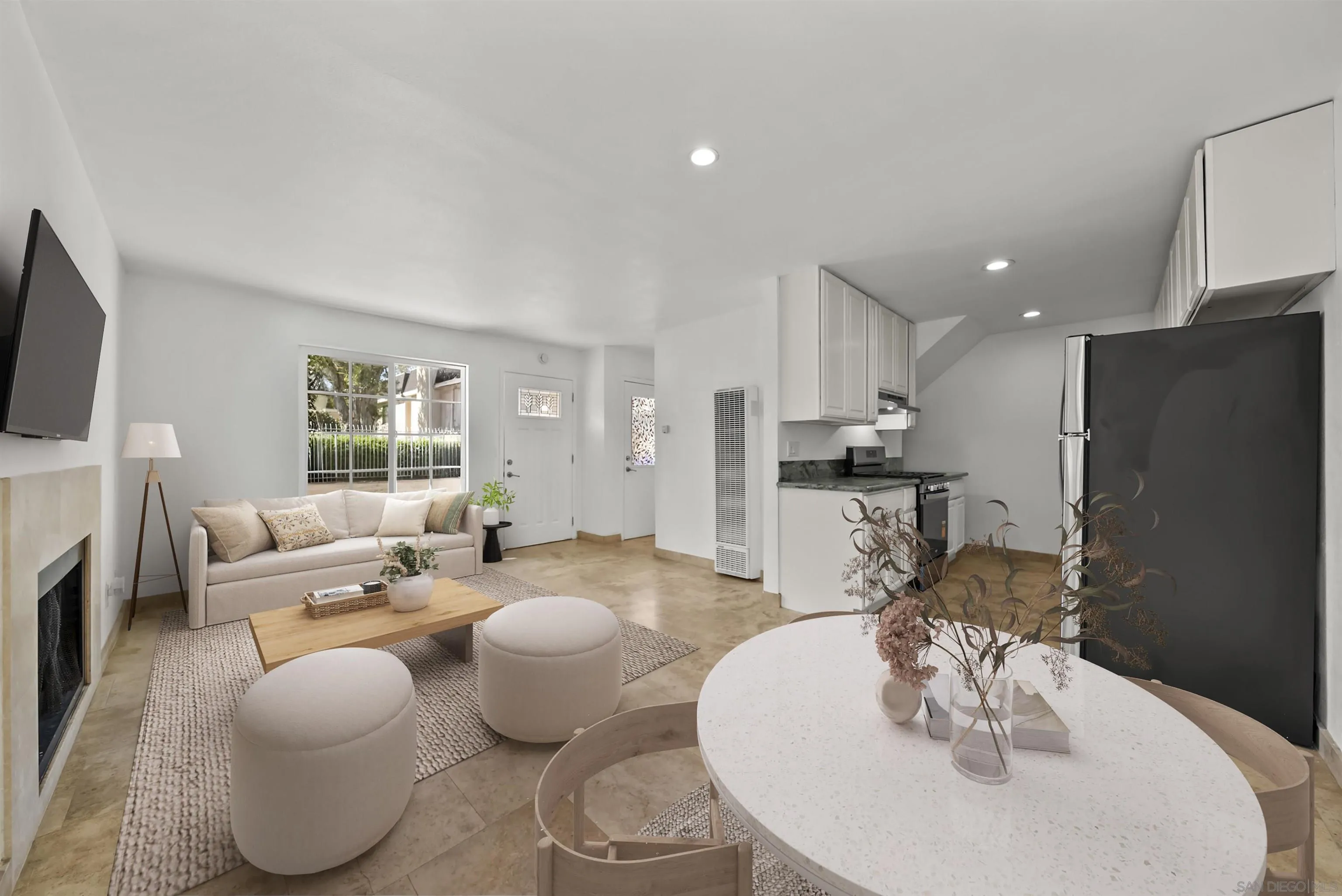 Open-plan living room and kitchen with a fireplace, beige sofa, white cabinets, and round dining table.