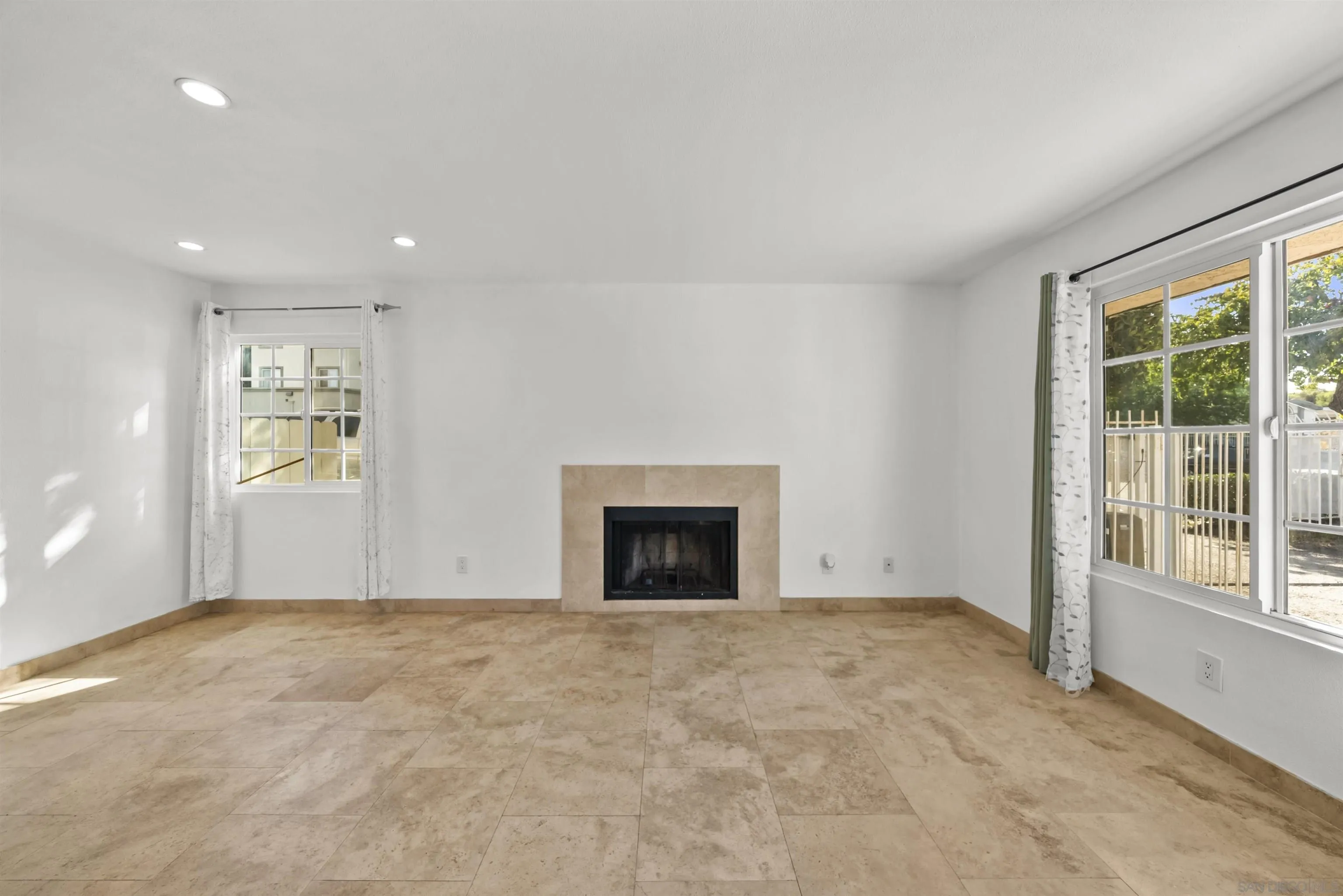Vacant living room with a tiled floor, central fireplace, and large windows.