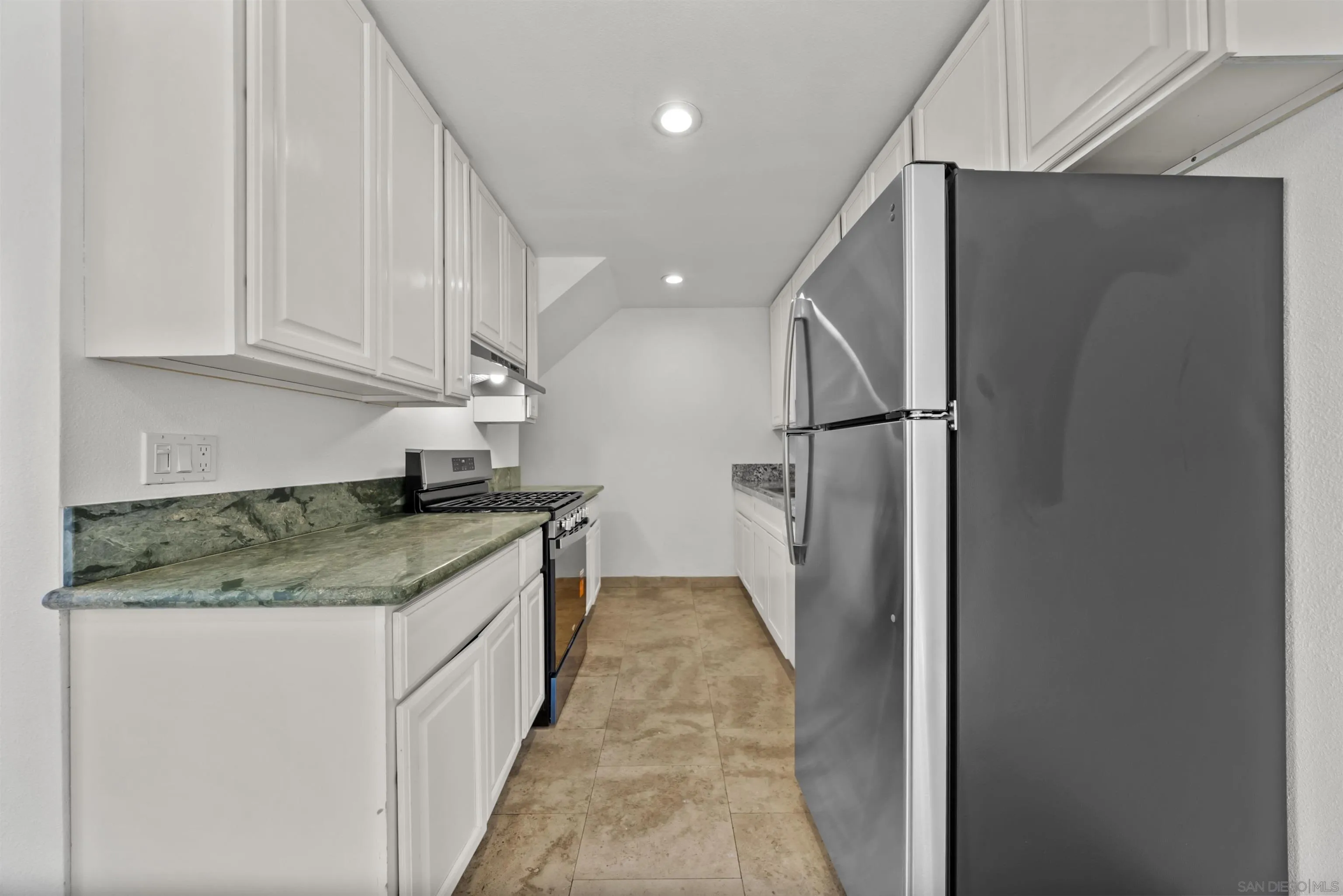 Galley kitchen with white cabinets, green stone counters, and stainless-steel appliances.