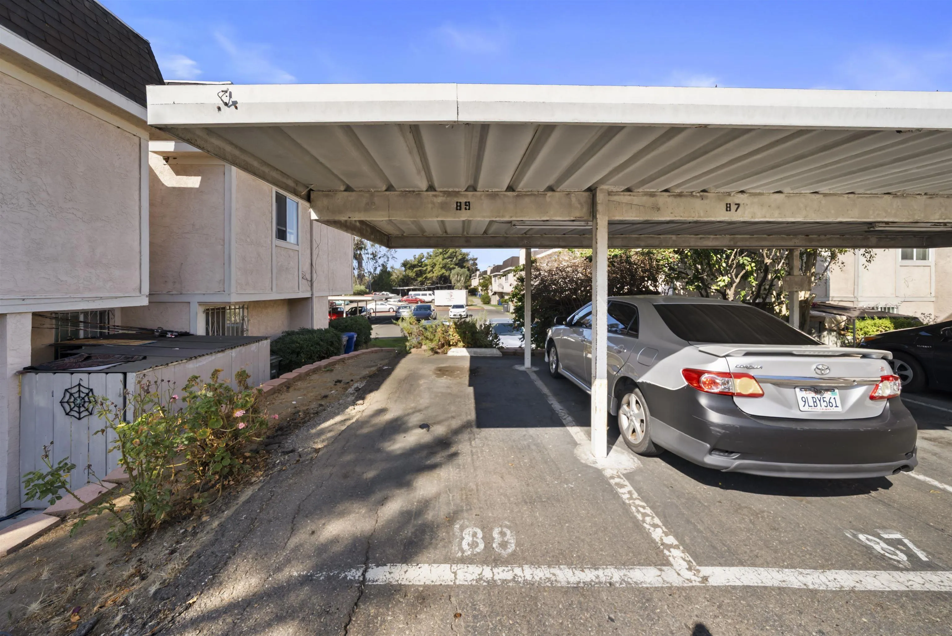 Covered parking area with numbered spaces and a silver sedan beside an apartment building.
