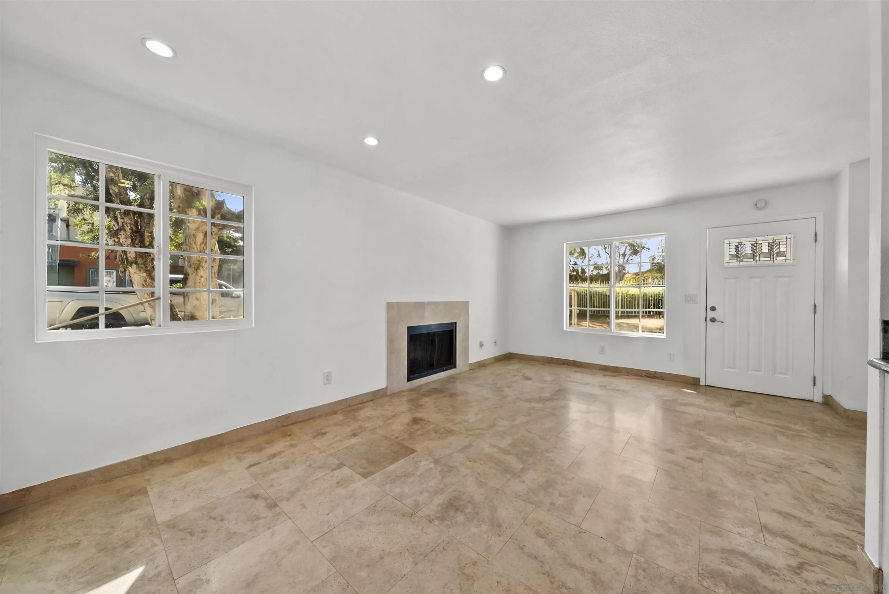 Empty living room with tan tile floors, a fireplace, and two grid-pane windows.