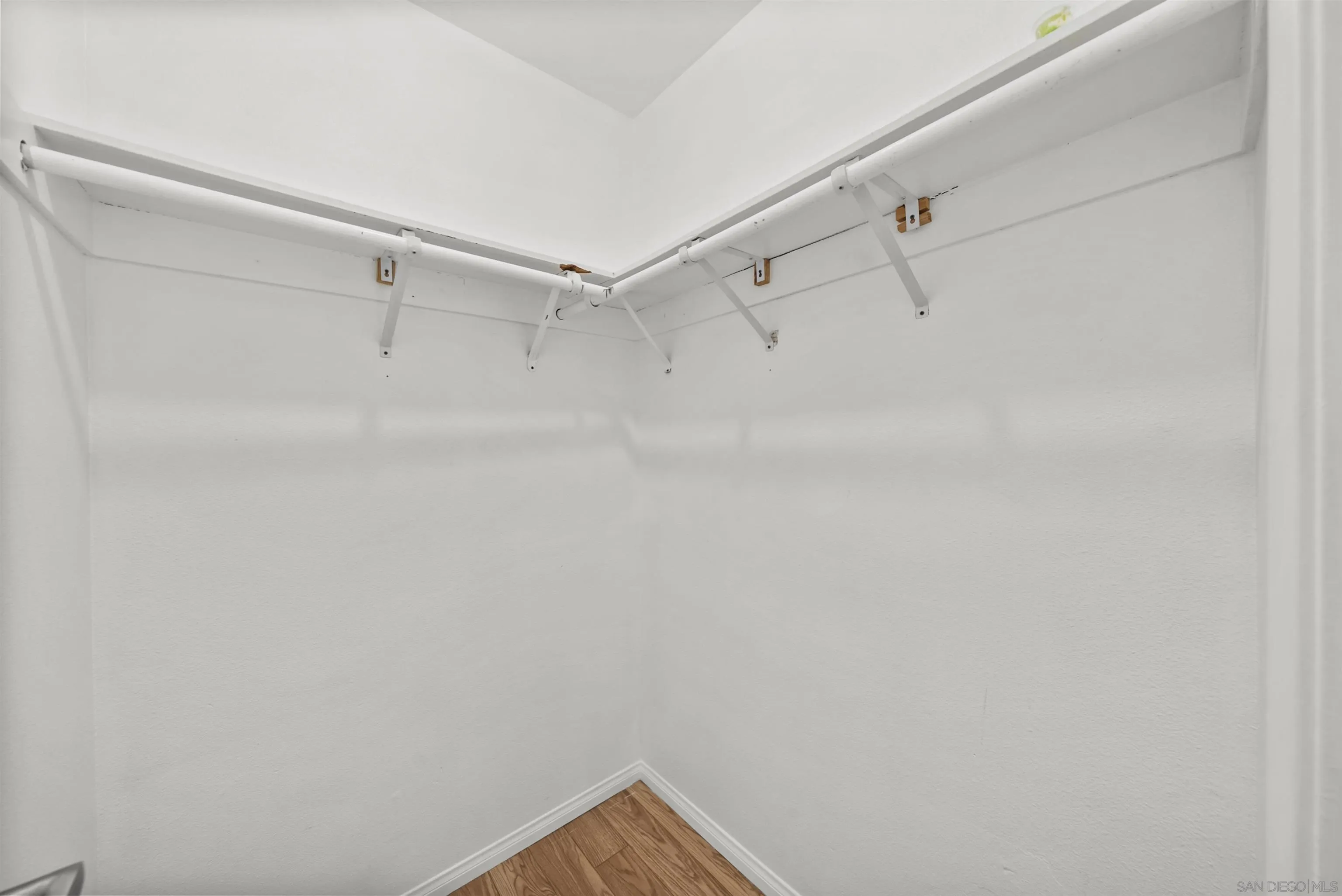 Small walk-in closet with wraparound hanging rods and wood-look flooring.