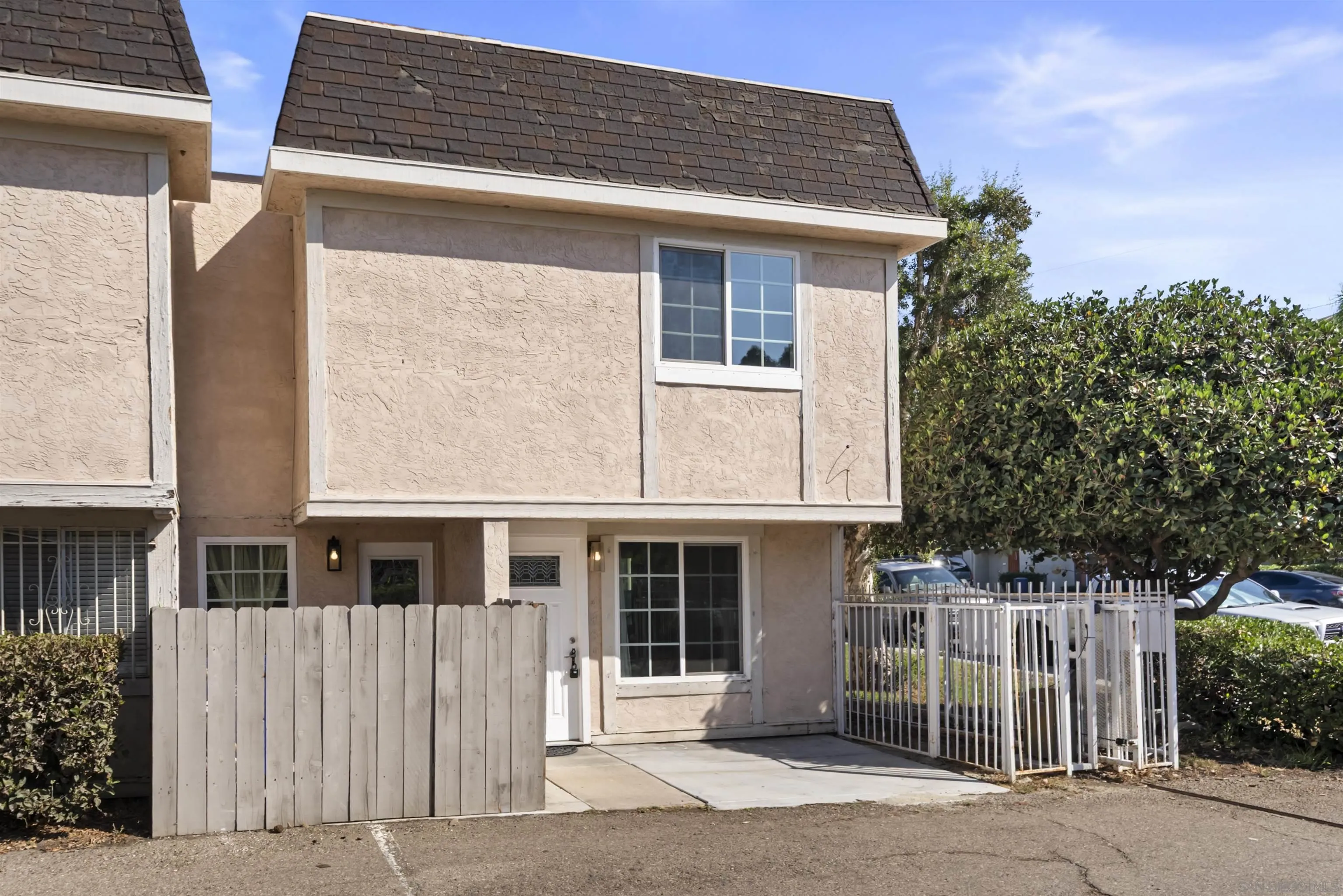 Two-story beige stucco home with a dark shingle roof and fenced concrete patio.