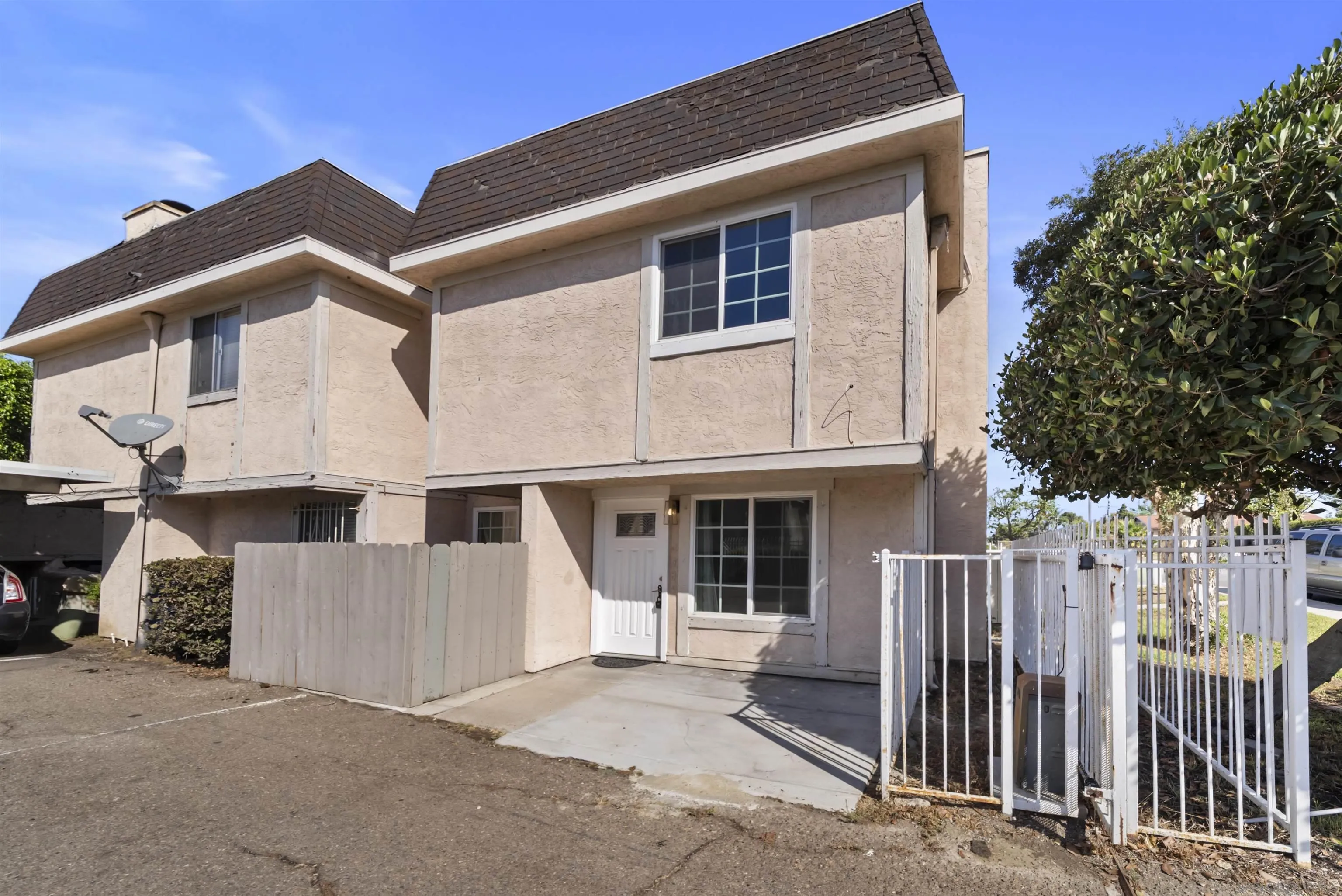 Two-story beige stucco residence with dark shingle roofs and a fenced concrete patio.