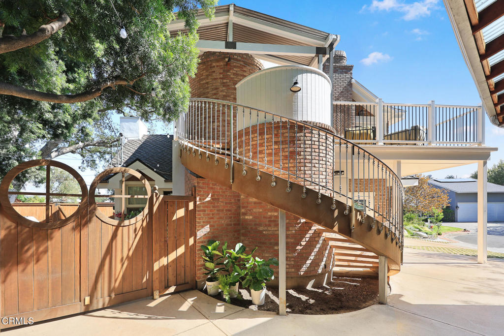 Brick home with a curved metal staircase, elevated deck, and wooden gate.