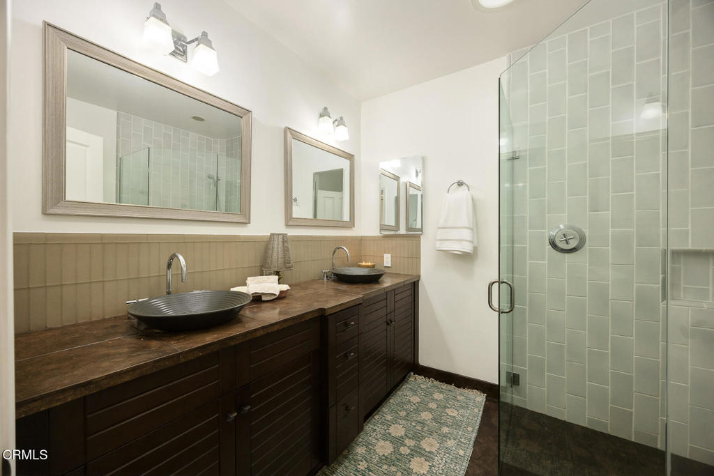 Bathroom with a double vessel-sink vanity and pale green tiled glass shower.