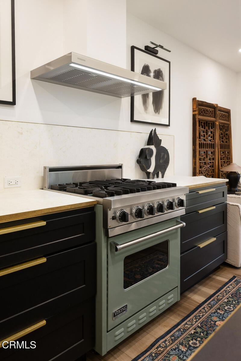 Kitchen with a stainless steel range, dark cabinets, brass pulls, and light stone counters.