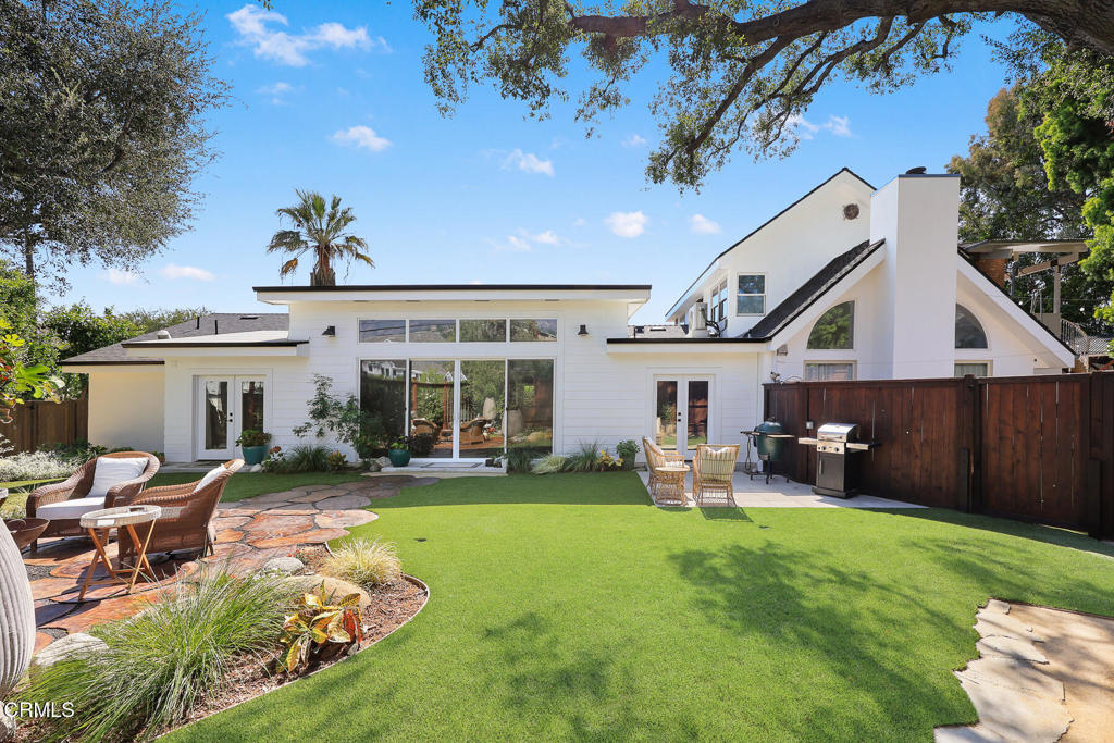 Home’s backyard with a broad lawn, stone patio seating, and outdoor grill.