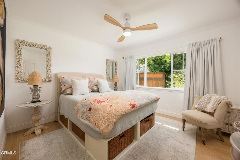 Bright bedroom with patterned bedding, woven bed storage, a ceiling fan, and a large window.