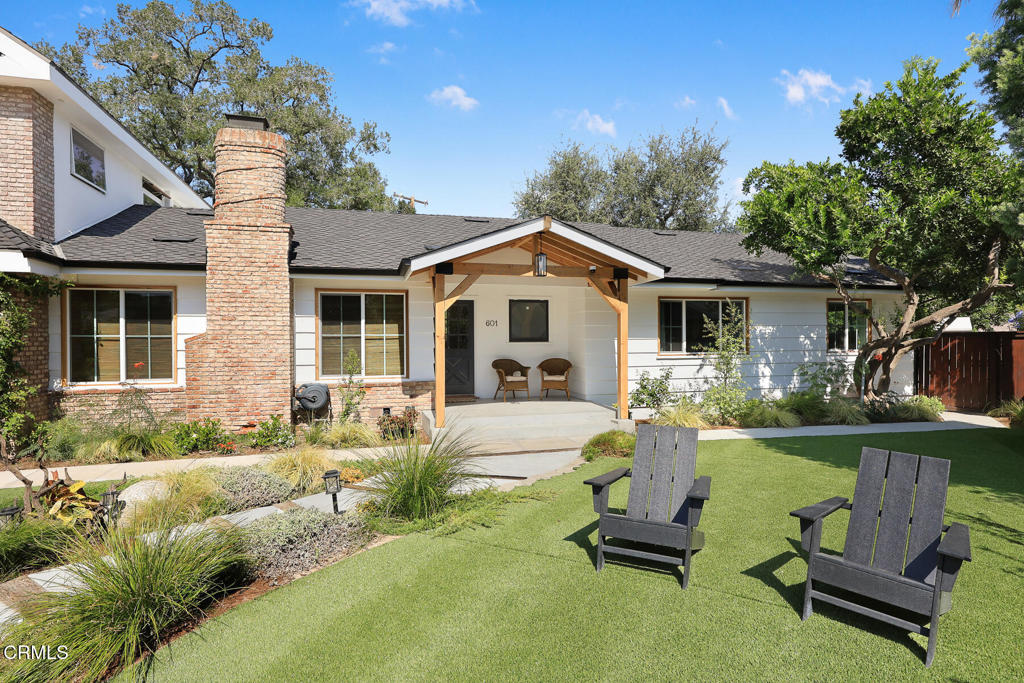 Single-story home with a brick chimney, covered entry, and two chairs on the lawn.