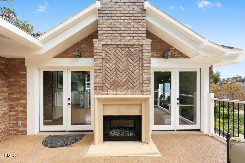 Covered patio with a brick fireplace between glass doors and a black metal railing.