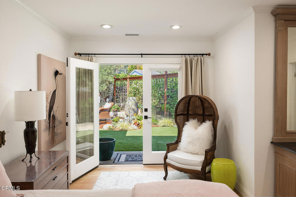 Bedroom with open French doors overlooking a landscaped yard and garden seating area.