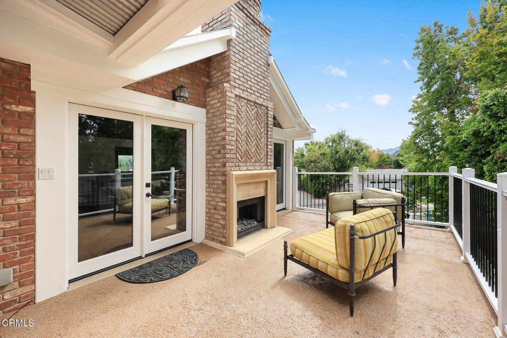 Outdoor patio with a brick fireplace, striped lounge chairs, and railing overlooking trees.