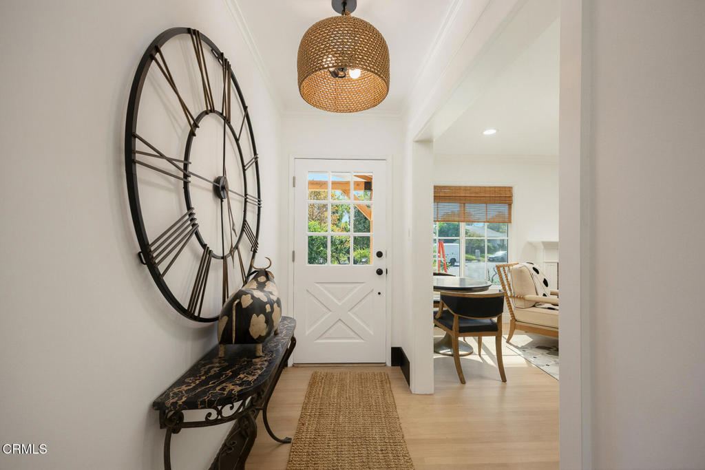 Furnished entry foyer with a large open-frame clock, woven pendant light, and glass-paneled front door.