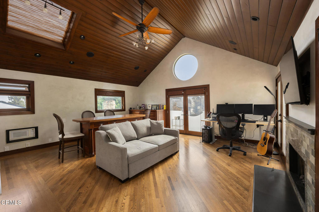 Living room with a vaulted wood ceiling, gray sofa, home office, and stone fireplace.