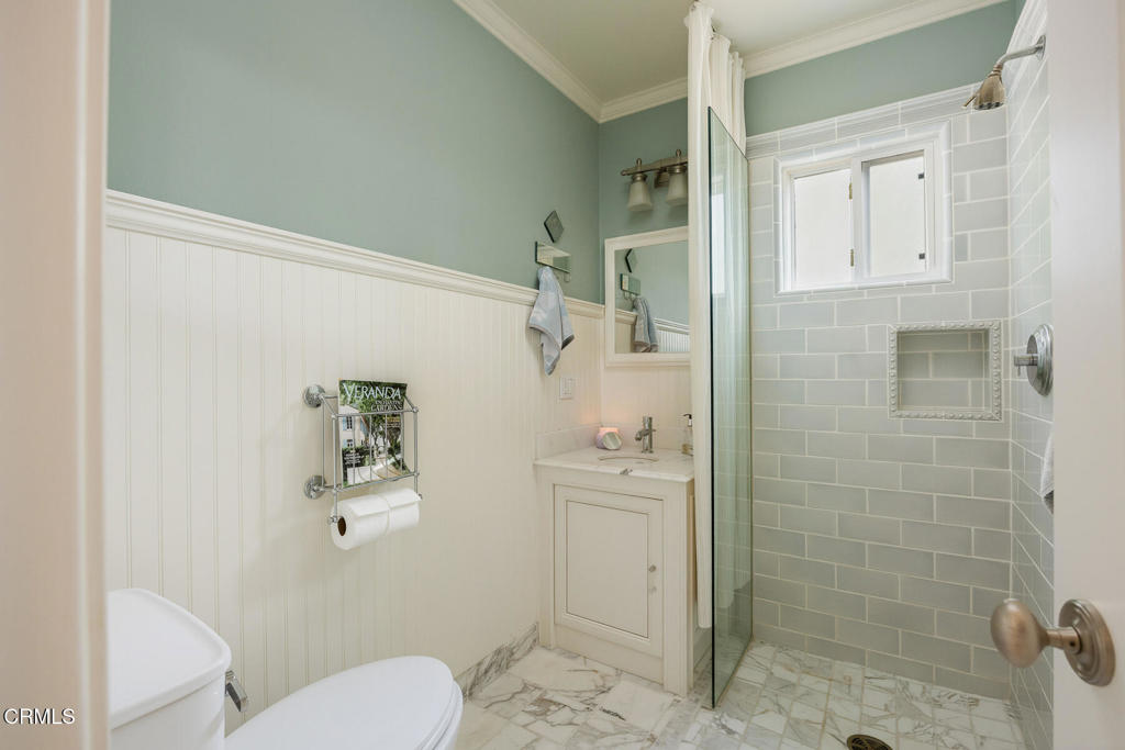 Bathroom with a glass shower, pale gray tile, white beadboard wainscoting, and marble-patterned flooring.