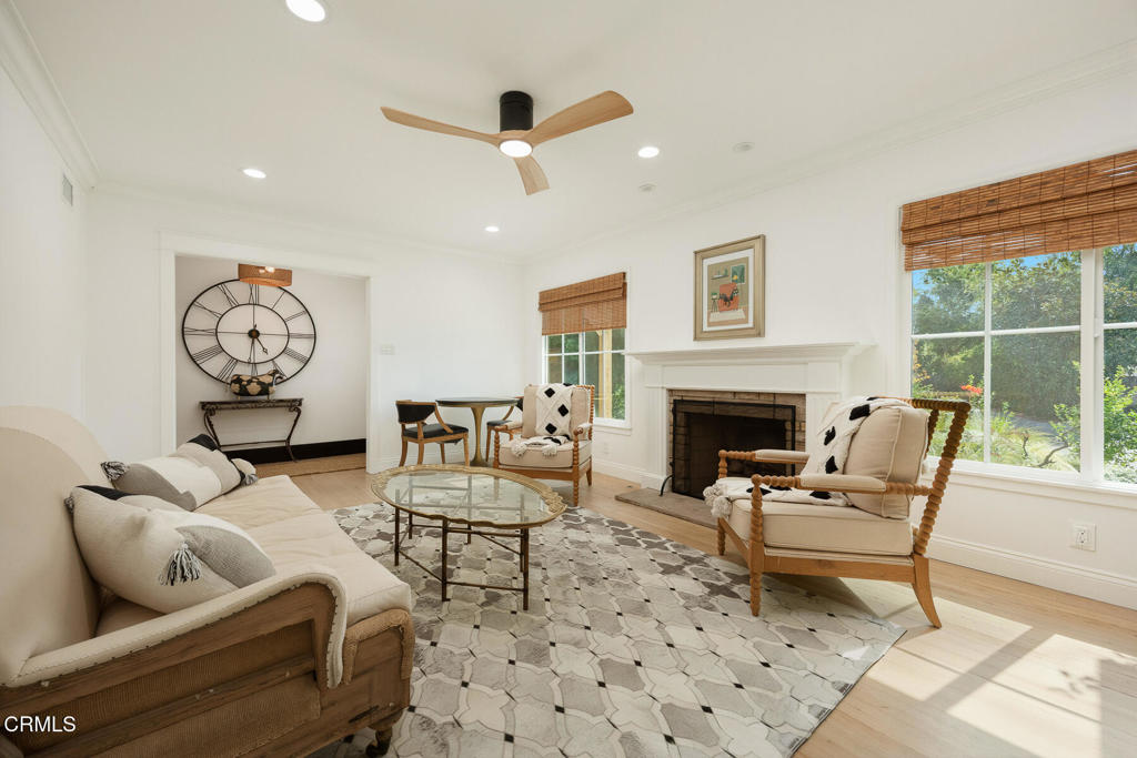 Furnished living room with a white fireplace, large garden-facing windows, and a seating area around a glass coffee table.