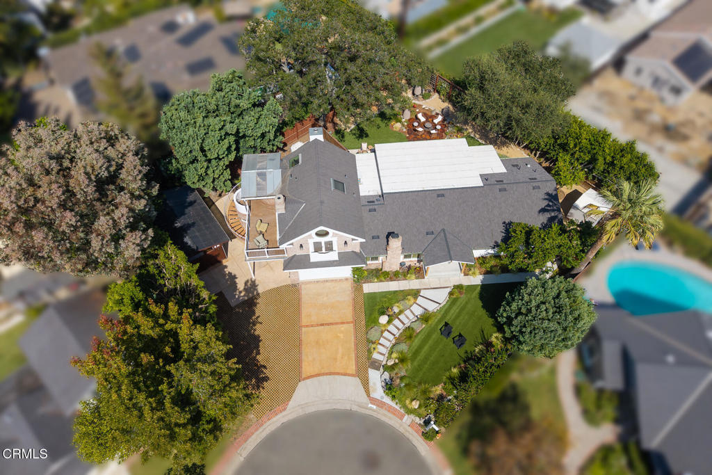 Aerial view of a home with a curved driveway, landscaped lawn, and backyard patio.