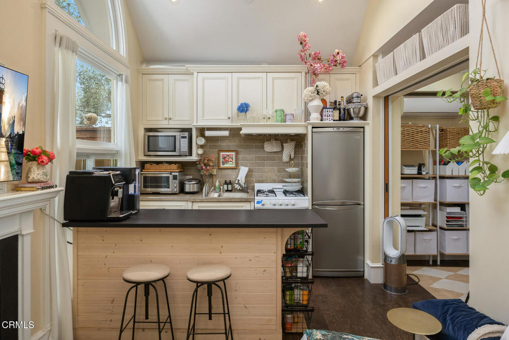 Kitchen with a black island counter, two stools, stainless appliances, and an adjoining pantry.