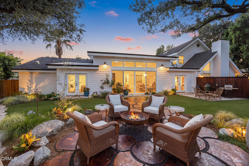 Modern home’s rear exterior at dusk, with illuminated windows and a landscaped patio centered on a fire pit.