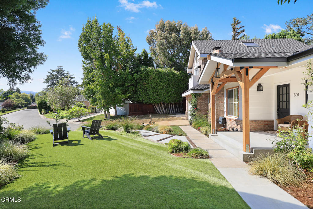 Home with a covered timber porch, landscaped lawn, and two chairs beside the walkway.