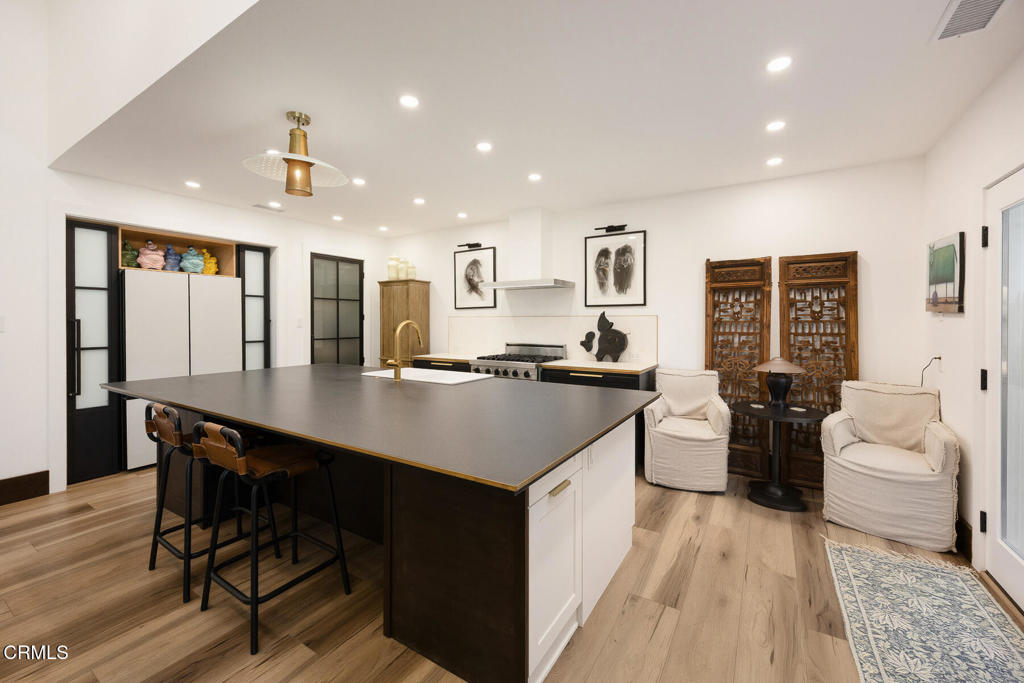 Bright kitchen with a large dark island, bar stools, and a pair of white lounge chairs.