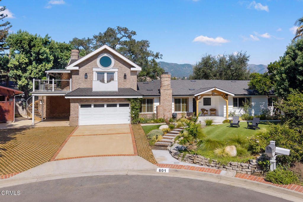 La Cañada Flintridge home with a brick gabled upper level, balcony, landscaped lawn, and mountain backdrop.