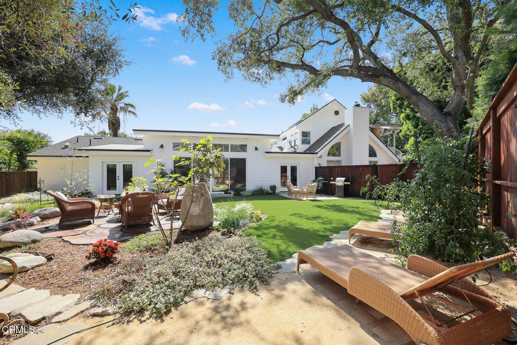 White home opening onto a landscaped backyard with artificial turf, stone patio, and outdoor seating.