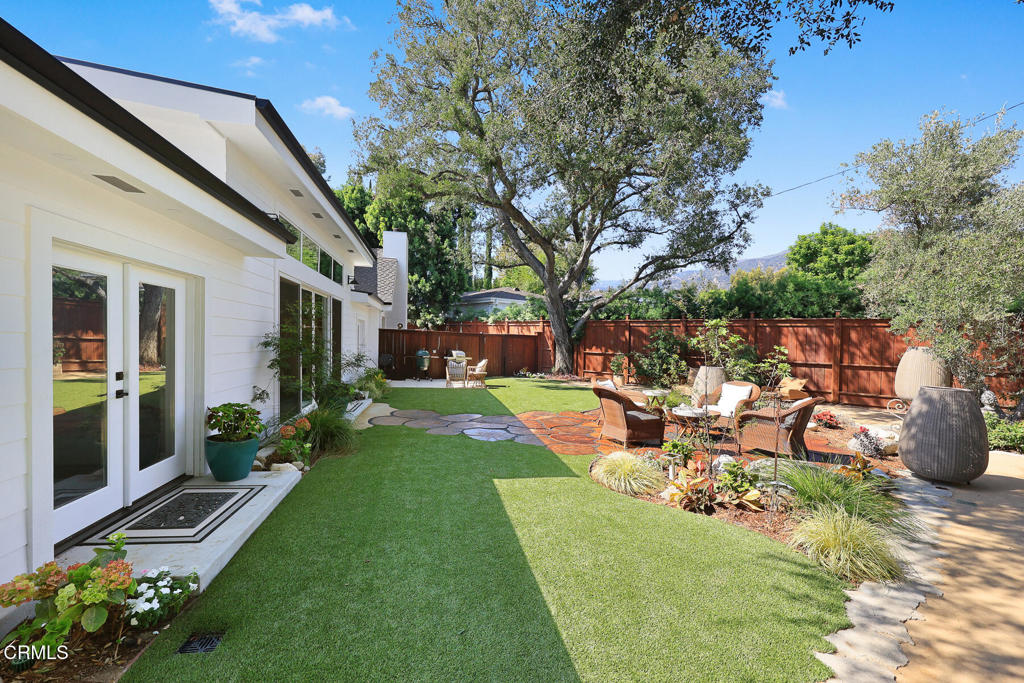 Backyard with a green lawn, landscaped seating patio, mature shade tree, and wooden privacy fence.