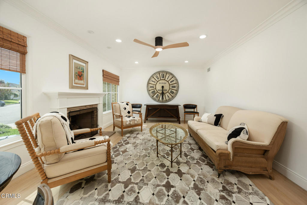Living room with a white fireplace, cream seating, patterned rug, and large Roman-numeral wall clock.