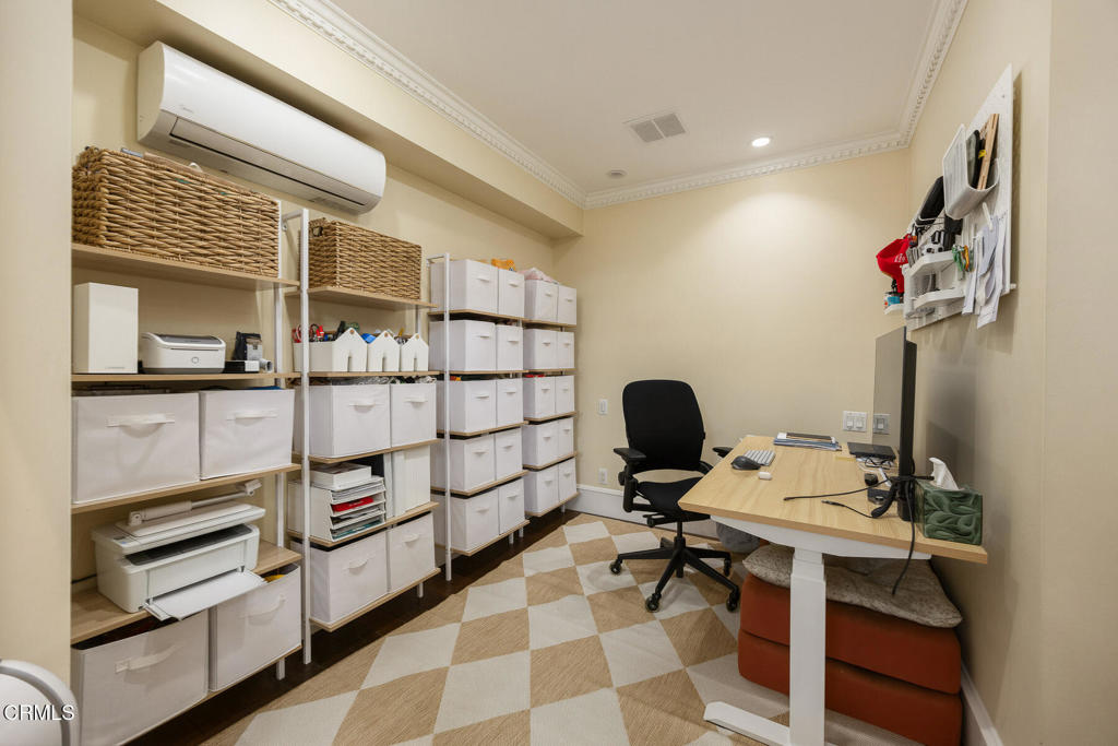 Home office with extensive storage shelving, a light wood desk, and a checkerboard rug.