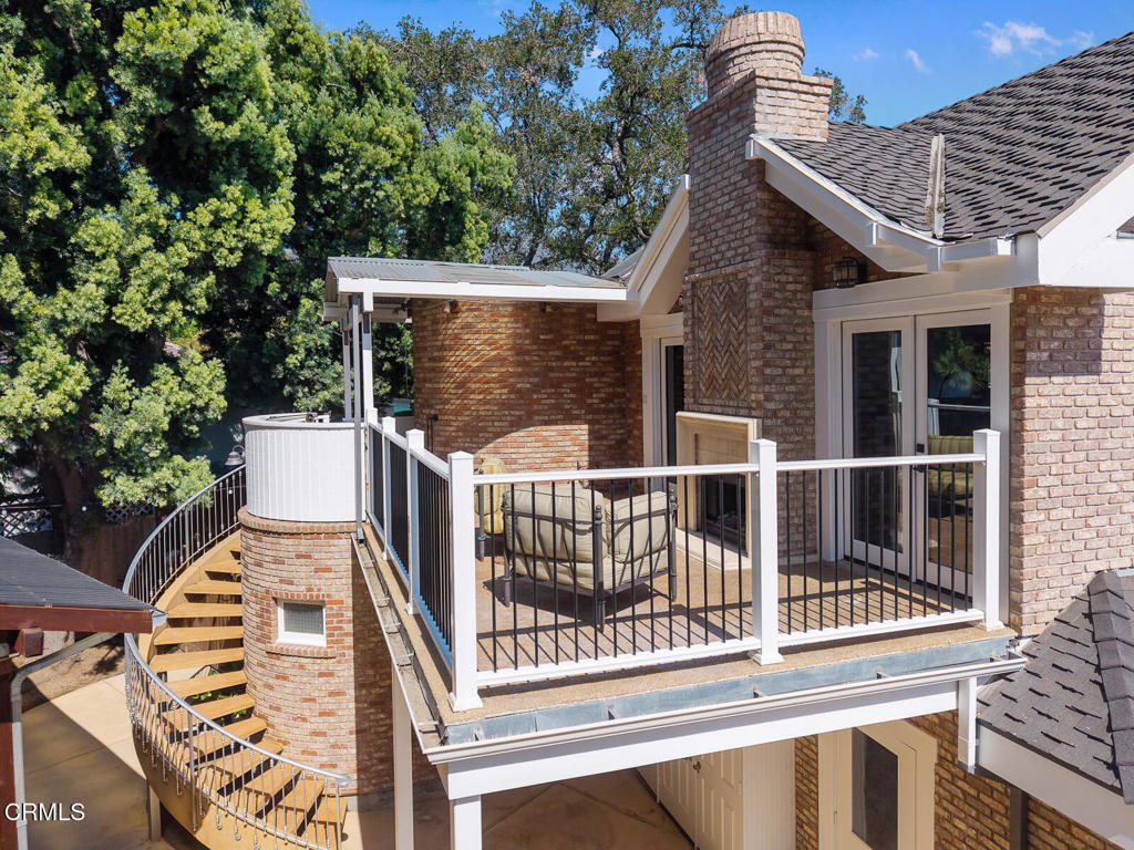 Elevated brick patio with covered seating, a round hot tub, and a curved staircase.