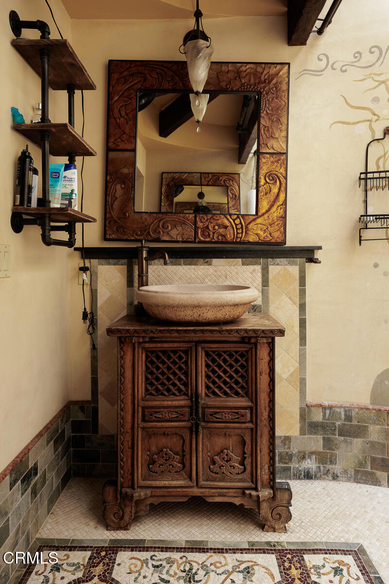 Bathroom vanity with a carved wooden cabinet, stone vessel sink, and ornate framed mirror.