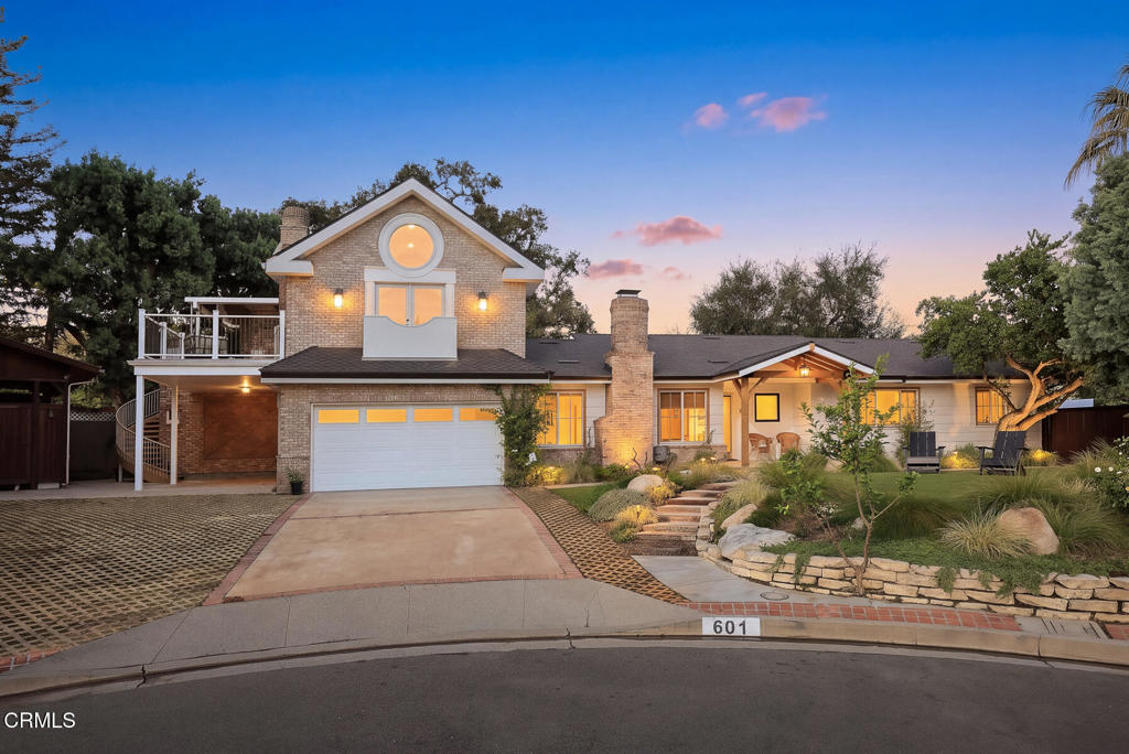 Two-story home at dusk with a brick facade, lit windows, and landscaped front yard.