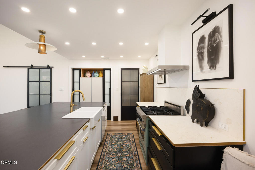 Renovated kitchen with a long island, brass fixtures, black-framed glass doors, and a patterned runner.