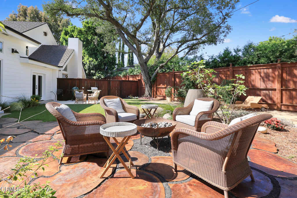 Backyard patio with wicker seating around a fire pit beneath a large shade tree.