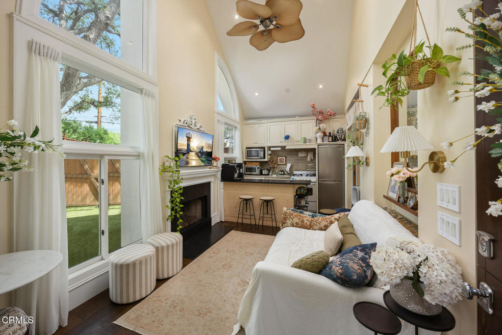 Living room with vaulted ceiling, tall windows, fireplace, and open kitchen.