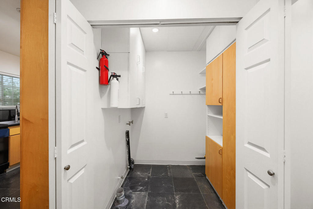 Utility room with dark tile flooring, built-in wood cabinets, wall hooks, and fire extinguishers.